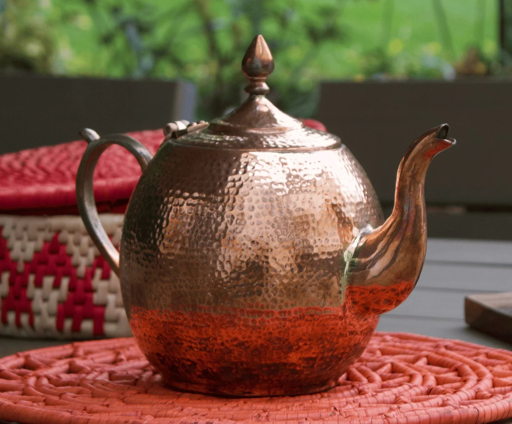Handcrafted hammered copper teapot on woven placemat, artisan Pakistani homeware