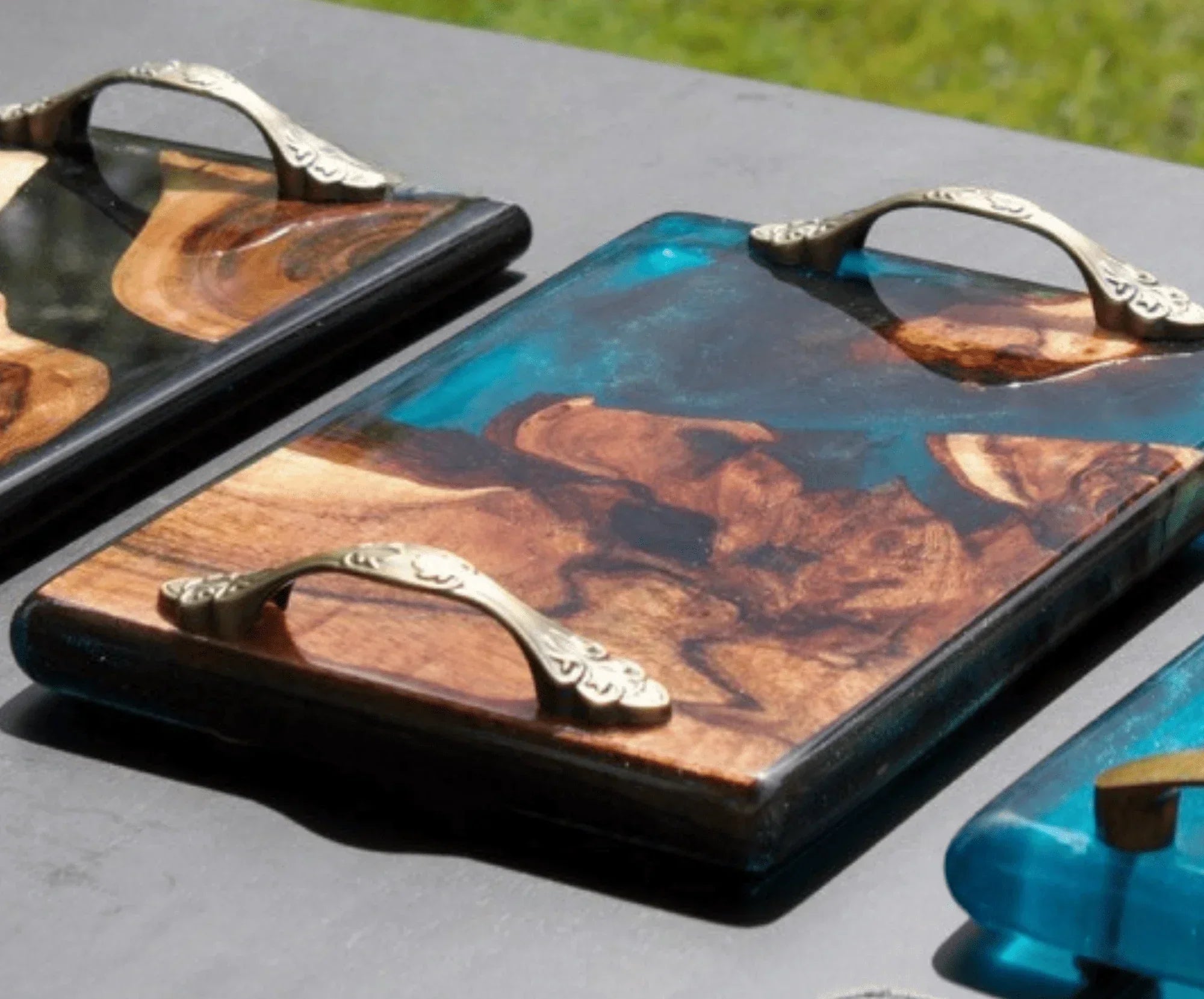 Handcrafted wood and resin serving trays with ornate brass handles on a table